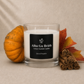 A clear glass jar candle with white wax and a black front label reading 'Alba Gu Bréth' and 'Spiced Pumpkin,' styled with a small orange pumpkin, autumn leaves, and cinnamon sticks on a beige textured background.
